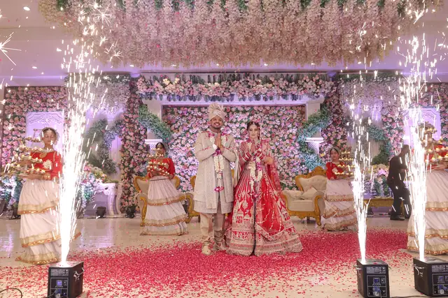 A bride and groom on a flower-covered stage, spark fountains on both sides and rose petals across the floor.